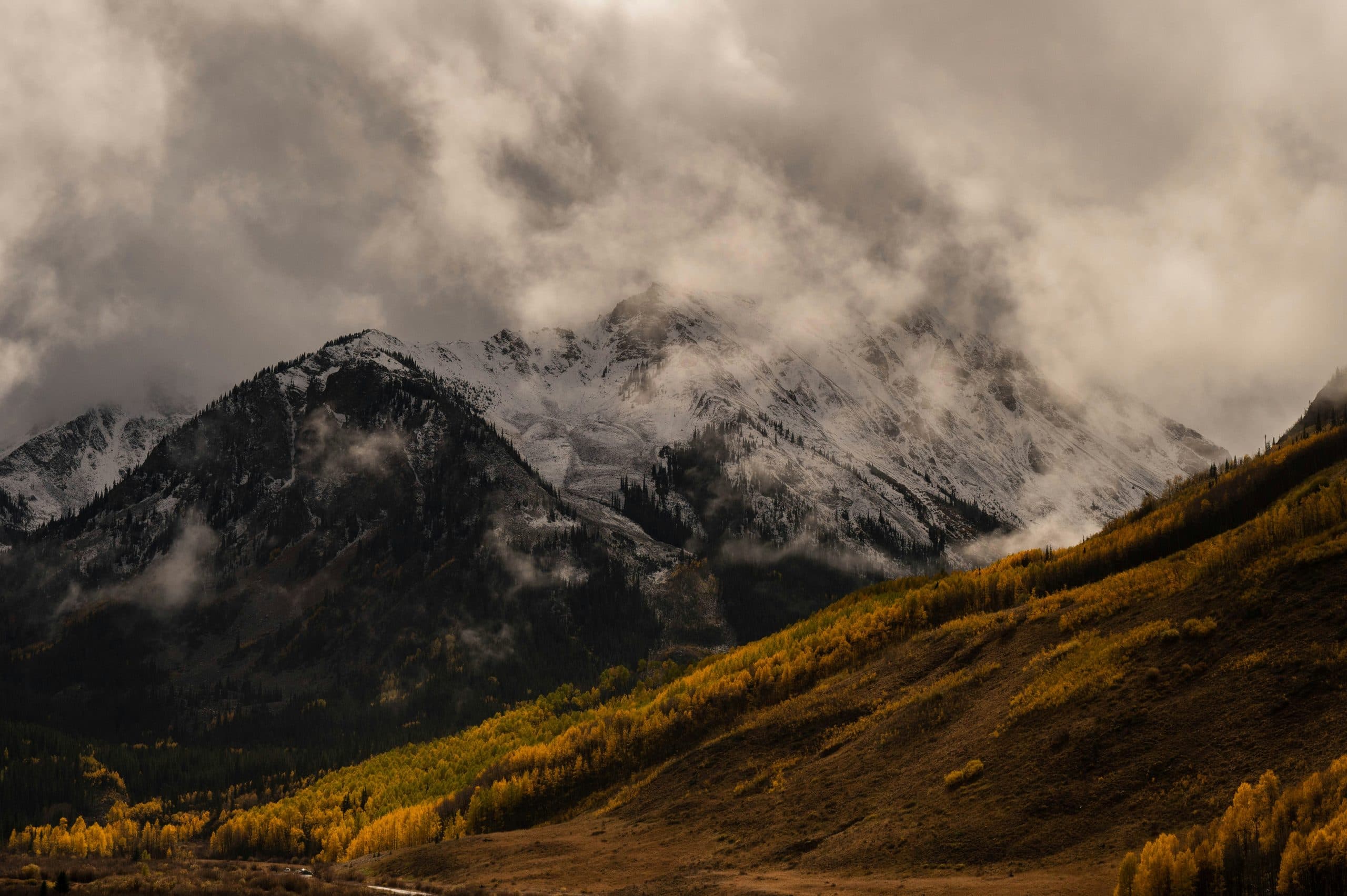 Storm cloud breaking over a snow-covered peak above a golden aspen slope